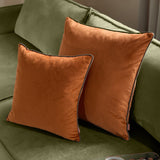 Two Meridian square velvet cushions in burnt pumpkin orange with mocha piped edges, styled on a green velvet sofa.