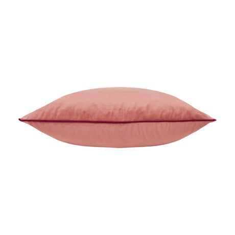 Meridian plain velvet cushion in coral pink, shown side-on with a contrasting burgundy piped edge trim, on a plain white background.