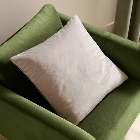 Meridian Plain Velvet Cushion in dove silver with charcoal piped edging, square velvet-feel design placed on a green upholstered armchair.