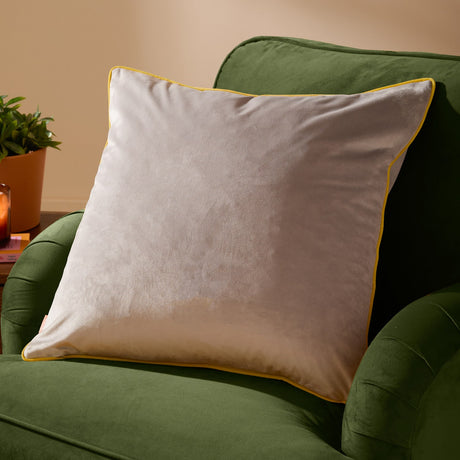 Meridian Plain Velvet Cushion in dove grey with contrasting bright yellow piped border, shown on a green velvet armchair in a living room setting.