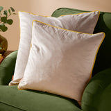Two square Meridian velvet cushions in dove grey with contrasting yellow piped edging, shown on a green upholstered sofa.