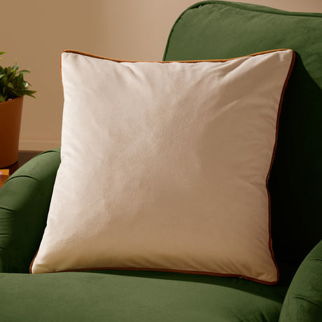 Meridian Plain Velvet Cushion in ecru with contrasting ginger piped edge, square scatter cushion shown on a green sofa.