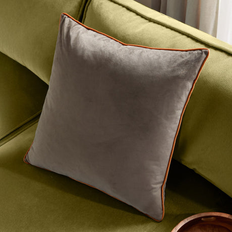 Meridian square velvet cushion in mocha brown with orange piped edging, shown resting on an olive green sofa.