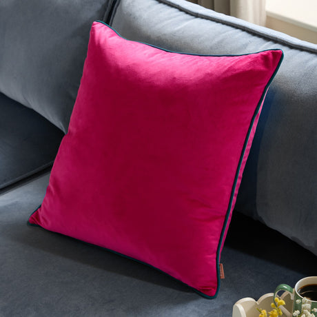 Meridian Plain Velvet Cushion in raspberry pink with contrasting teal piped edge, square velvet fabric design, shown propped on a grey sofa.