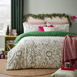 Merry Christmas cotton duvet cover set on a bed, oat ground with green hand-drawn festive motifs, reversed edge showing green polka dot design, styled with pink cushions in a bedroom.