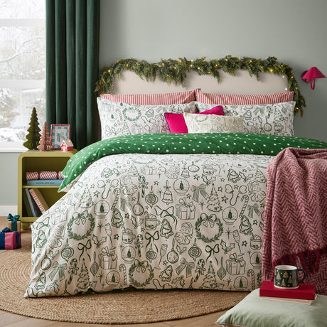 Merry Christmas cotton duvet cover set on a bed, oat ground with green hand-drawn festive motifs, reversed edge showing green polka dot design, styled with pink cushions in a bedroom.