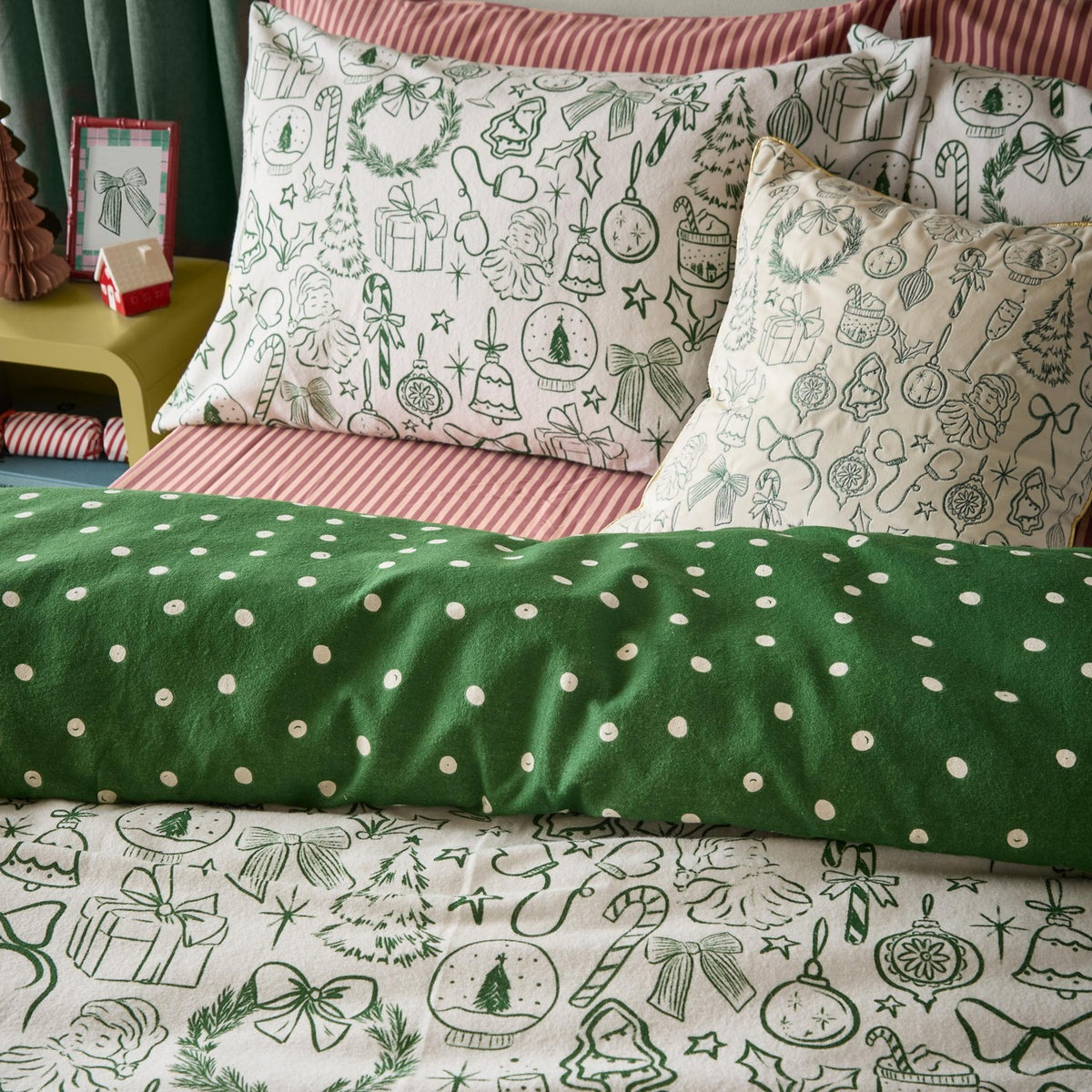 Merry Christmas cotton duvet cover set on a bed, reversible design with green polka dots on one side and hand-drawn festive icons on oat cotton, styled with matching printed pillowcases and cushions.