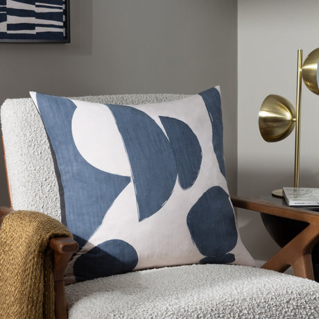 Meta Abstract Cotton Cushion in Dusk, cream cushion with bold blue-grey abstract shapes, styled on a boucle armchair beside a brass lamp.