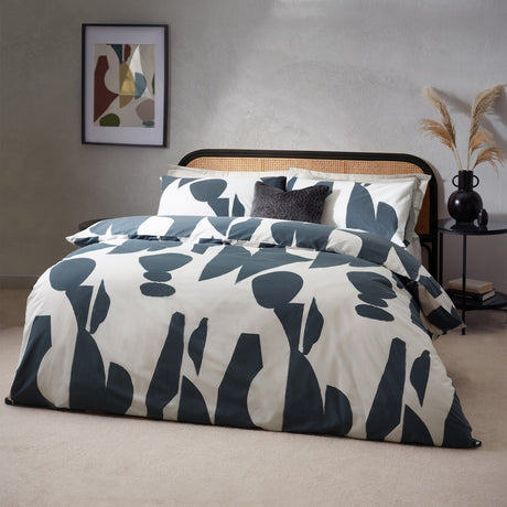 Meta Cotton Abstract Duvet Cover Set in Dusk, dressing a cane headboard bed with matching pillowcases in a slate blue and cream abstract print, styled in a modern bedroom.
