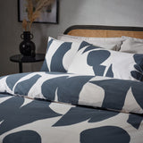Meta Cotton Abstract Duvet Cover Set in Dusk, featuring a large-scale slate blue abstract print on off-white cotton-rich fabric, shown with matching pillowcases on a bed in a bedroom setting.