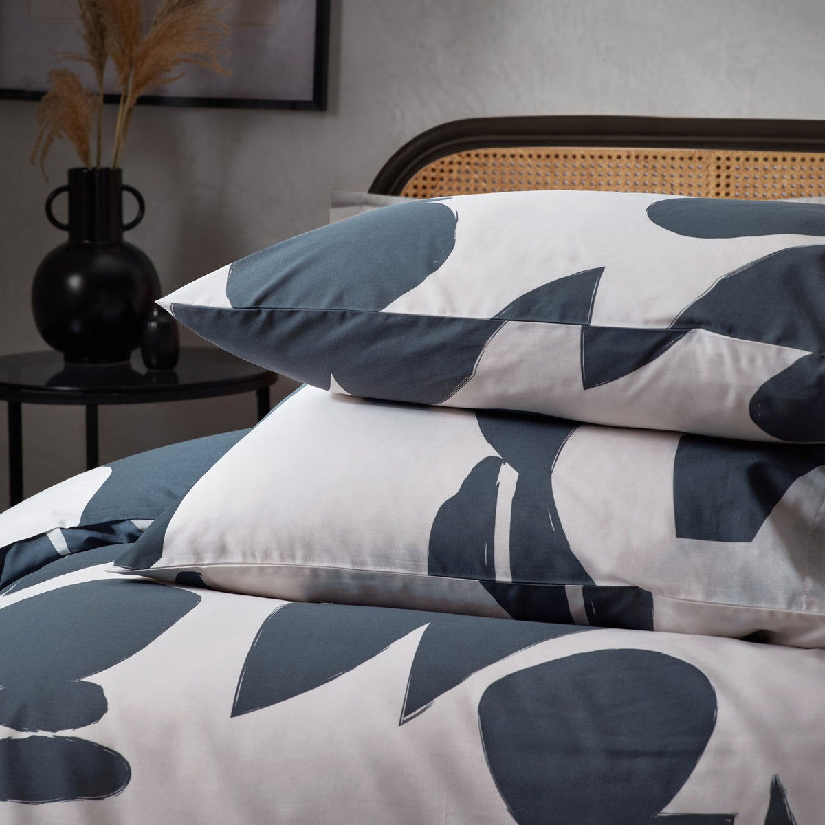 Cotton Abstract Duvet Cover Set in Dusk featuring off-white bedding with a slate blue abstract print on the duvet cover and matching pillowcases, styled on a bed with a rattan headboard.