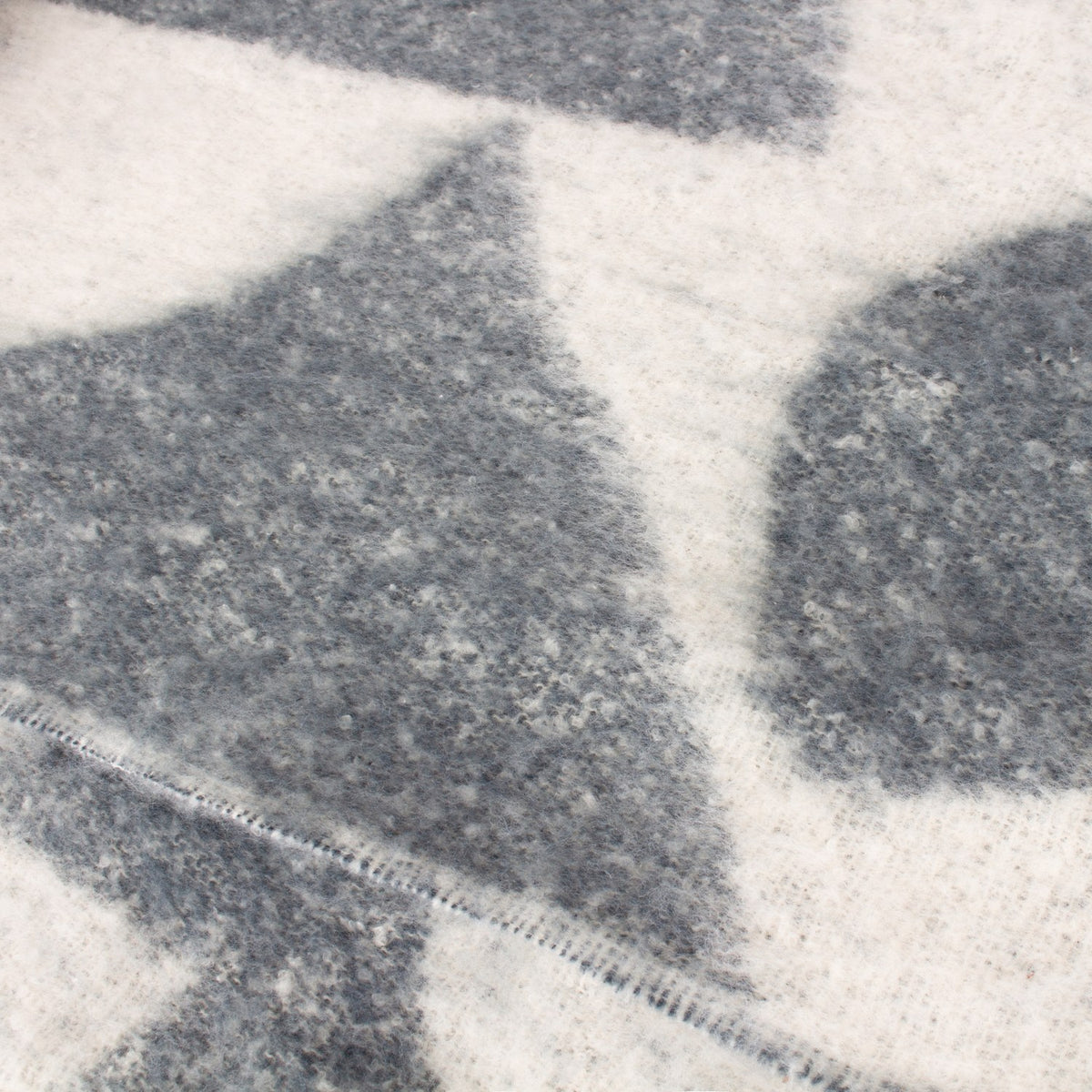 Close-up of the Meta Jacquard Polyester Throw in Dusk, showing soft blue-grey abstract shapes on a cream faux mohair fabric with a visible stitched edge.