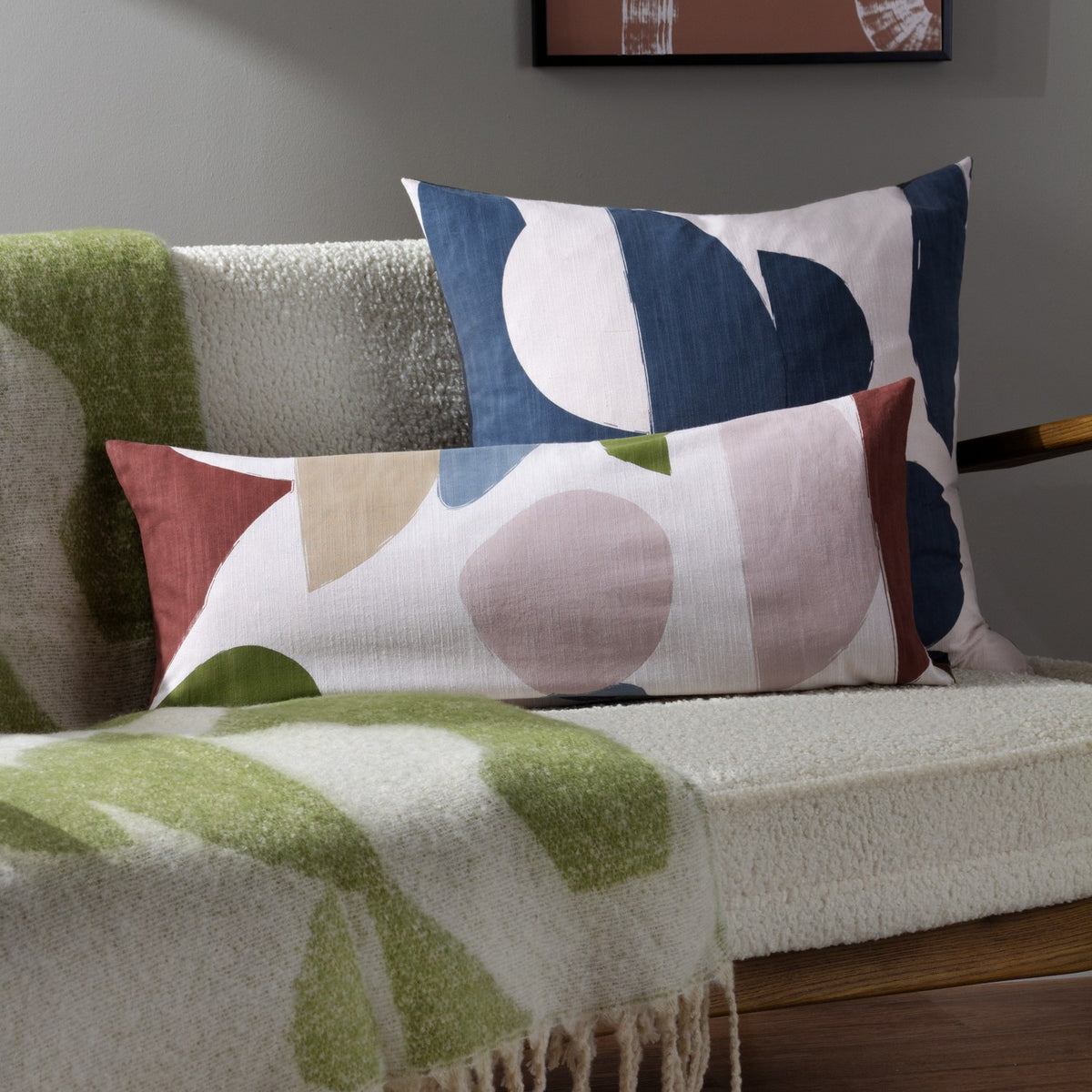 Meta Jacquard Polyester Throw in olive and cream draped over a boucle sofa, with matching rectangular cushions in navy, blush, and rust tones nearby.