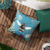 Midnight Garden Animal Polyester Cushion in teal, featuring a detailed bee print with country flowers, shown on a wooden deck beside a green outdoor cushion.