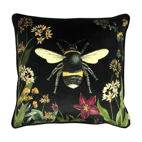 Square black velvet cushion featuring a large printed bumblebee, bordered by botanical stems, cream and amber blooms, and a red flower, shown on a plain white background.