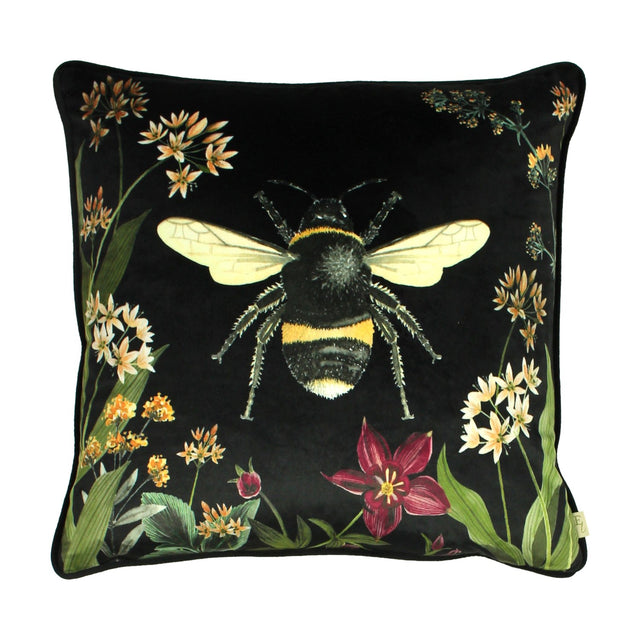 Square black velvet cushion featuring a large printed bumblebee, bordered by botanical stems, cream and amber blooms, and a red flower, shown on a plain white background.