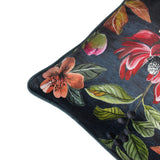 Corner detail of the Midnight Garden Floral Velvet Cushion in grey, showing painterly red and coral blooms, green foliage and dark berries on a deep grey velvet ground with piped edge.
