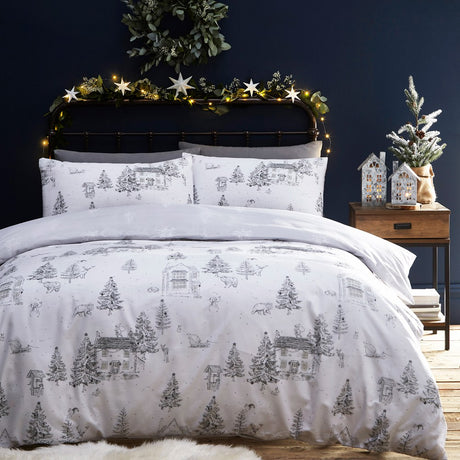 Midwinter Toile Printed Woodland Duvet Cover Set in Snow, white bedding with grey line-drawn cottages, firs and woodland animals, styled on a bed in a dark bedroom with festive lights.