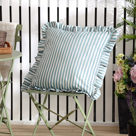 Millie Ruffle Striped Polyester Cushion in duck egg blue and cream, square with ruffled edge trim, shown on a green folding chair in an outdoor garden setting.