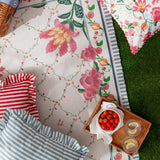 Millie Ruffle Striped Polyester Cushion in duck egg blue and cream, with ruffle-trimmed edges, shown on a floral picnic blanket alongside a red striped cushion and strawberry tray.
