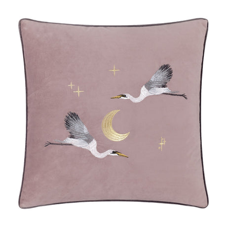 Moonlit Flight square velvet cushion in dusty pink, embroidered with two grey and white storks, a gold crescent moon, and scattered stars, with dark grey piped edging, shown on a white background.