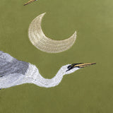 Close-up of the Moonlit Flight velvet cushion in olive green, showing embroidered heron head, neck and plumage beneath a gold crescent moon.