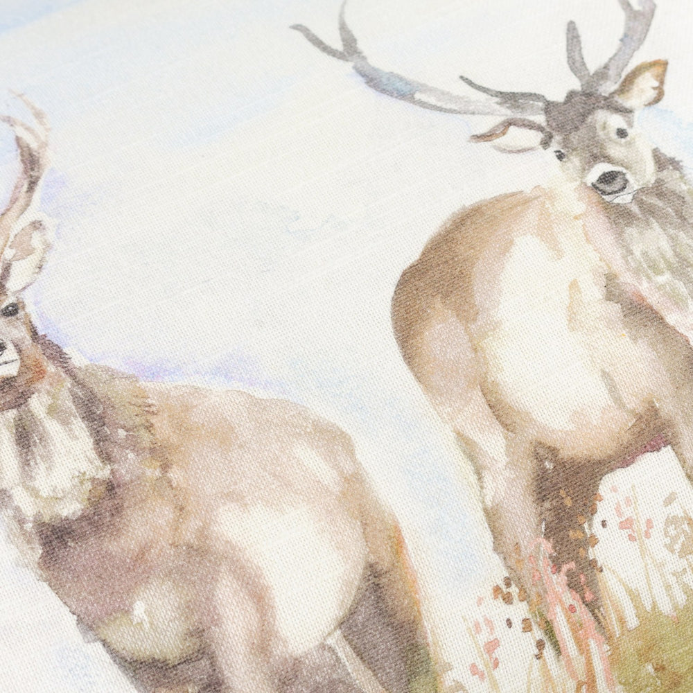 Close-up of the Moorland Stag Reversible Linen Cushion in Nut, showing hand-painted watercolour stags in cream and brown tones against a pale sky on a linen-cotton blend fabric.
