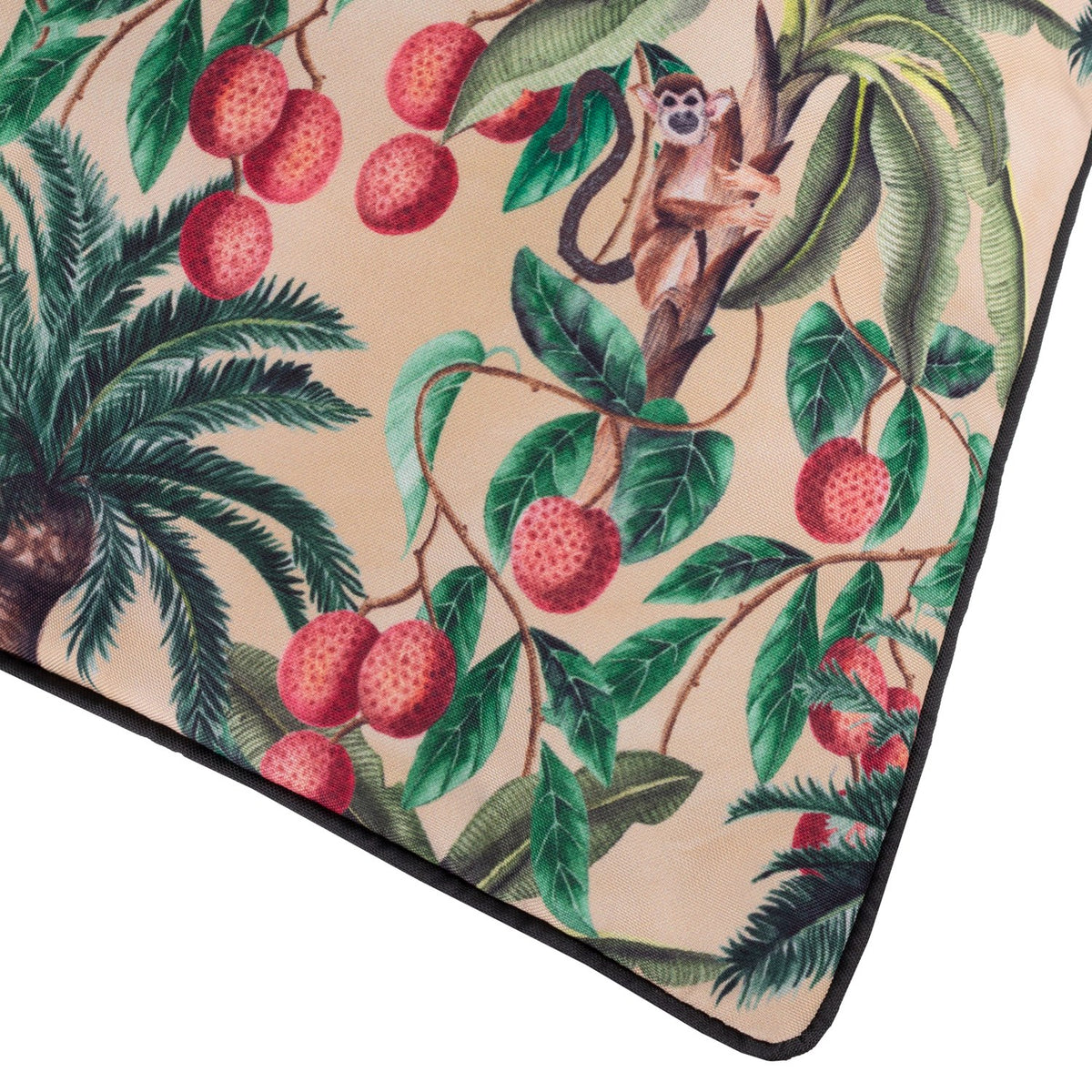 Corner detail of the Monkey Palm reversible polyester cushion in Papyrus, showing a beige tropical print with lychees, palm leaves and a monkey, edged in black piping.