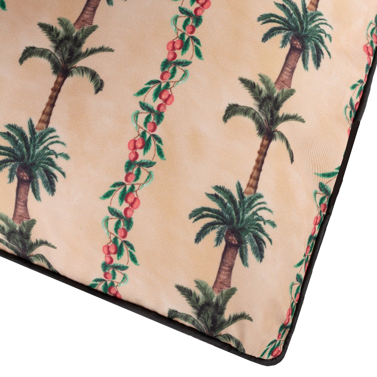 Corner detail of the Monkey Palm Reversible Polyester Cushion in Papyrus, showing green palm trees and red berry vines on a beige ground with black piped edging.