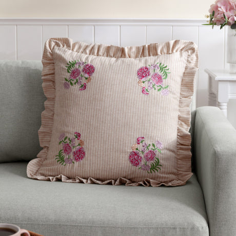 Martha Floral Linen Cushion in pink, 50x50cm with oatmeal stripe fabric, ruffled edge trim and corner floral embroidery, shown on a grey sofa.