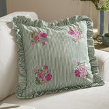 Martha Floral Linen Cushion in sage-and-cream ticking stripe with corner floral embroidery and ruffled edge, shown on a sofa in a living room.