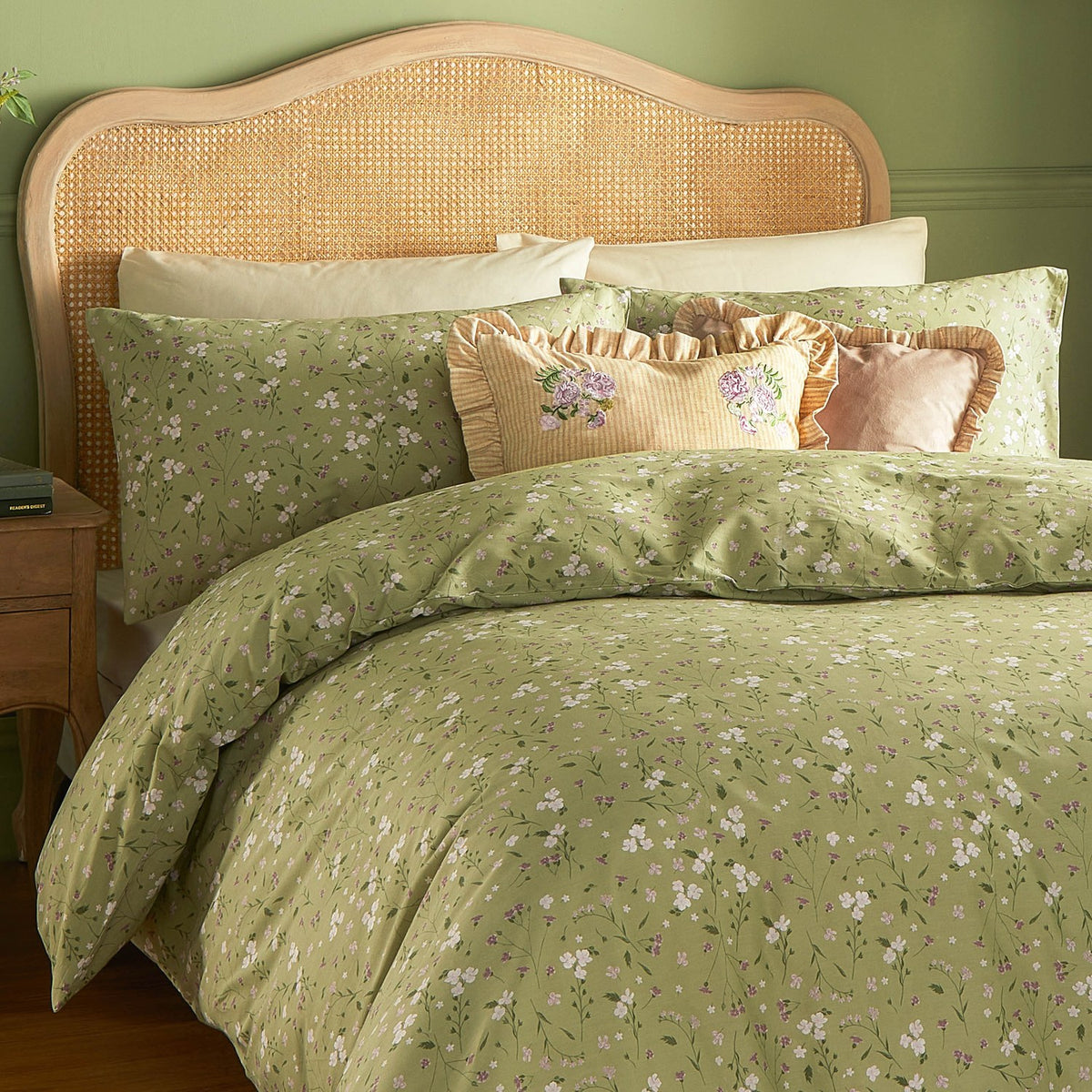 Martha Floral Linen Cushion in yellow-and-cream stripe with pink floral embroidery, styled on a green floral bed with matching pillows and headboard.