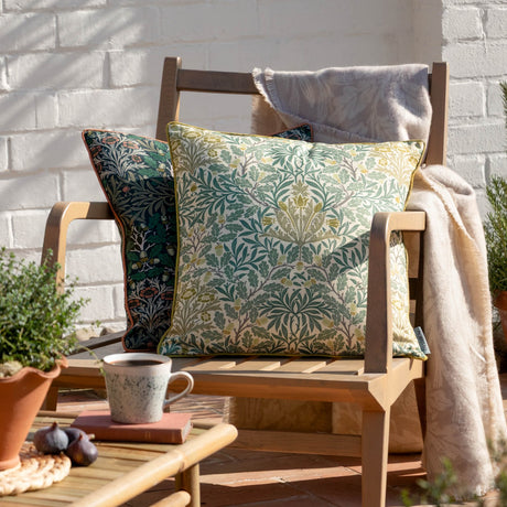 Multi Acorn Woodland polyester cushion in sage green and stone on a cream ground, with matching piped edges, styled on a wooden garden chair.