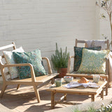 Multi Acorn Woodland polyester cushion in sage and stone green with cream piping, styled on wooden garden chairs alongside a matching cushion and outdoor seating area.