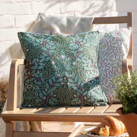 Multi Acorn Woodland square cushion in Thyme/Forest green with acorn and oak leaf print, shown on a wooden garden bench beside a matching lighter-toned cushion.