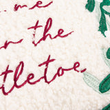 Close-up of the Mistletoe Wreath Embroidered Velvet Cushion, showing cream boucle fabric with "kiss me under the mistletoe" embroidered in red script beside green mistletoe leaves.