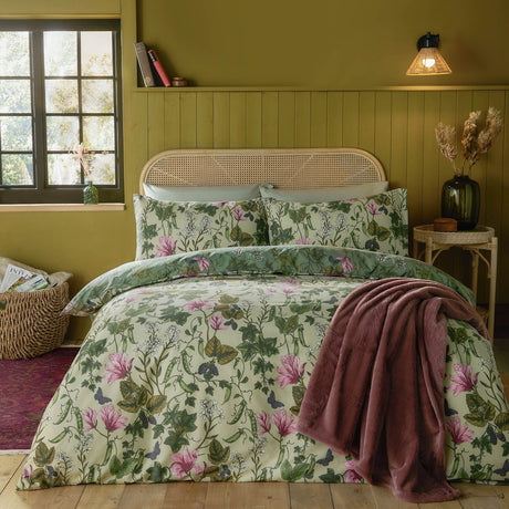 Mystic Berry reversible floral duvet cover set in green, shown on a bed with cream and pink botanical print, matching pillowcases, and a pink throw in a bedroom setting.