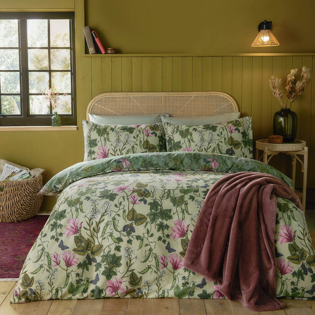 Mystic Berry reversible floral duvet cover set in green, shown on a bed with cream and pink botanical print, matching pillowcases, and a pink throw in a bedroom setting.