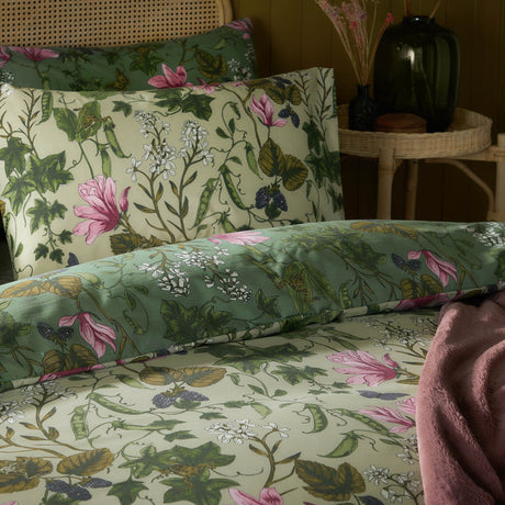 Mystic Berry reversible floral duvet cover set on a bed, showing cream and sage green sides with pink magnolias, ivy and pea pod print, styled with a matching pillowcase.