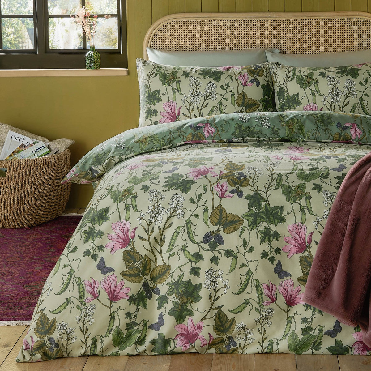 Mystic Berry Reversible Floral Duvet Cover Set in green on a bed with rattan headboard, cream ground with pink magnolias, ivy and pea pod print, styled in a bedroom.