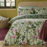 Mystic Berry Reversible Floral Duvet Cover Set in green on a bed with rattan headboard, cream ground with pink magnolias, ivy and pea pod print, styled in a bedroom.