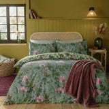 Mystic Berry Reversible Floral Duvet Cover Set in sage green with pink magnolias and ivy print, styled on a bed with matching pillowcases in an olive-toned bedroom.