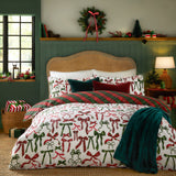 Nathalie Festive Bows Check duvet cover set in berry red and pine green, styled on a bed with plaid reverse, cushions and a teal throw in a festive bedroom setting.