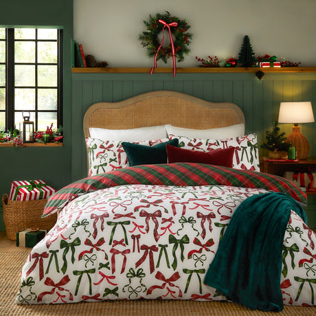 Nathalie Festive Bows Check duvet cover set in berry red and pine green, styled on a bed with plaid reverse, cushions and a teal throw in a festive bedroom setting.