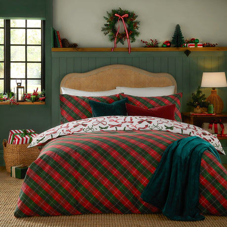 Nathalie Festive Bows Check duvet cover set on a bed, showing the red and green tartan check side with cream overcheck, paired with a bows-print pillowcase, in a festive green bedroom.