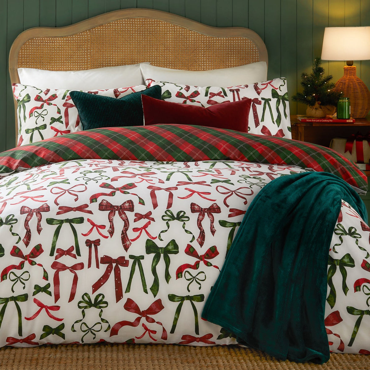 Nathalie Festive Bows Check Duvet Cover Set in Berry/Pine on a bed, showing the white bow-print side reversed to red and green tartan check, with matching pillowcases and styling.