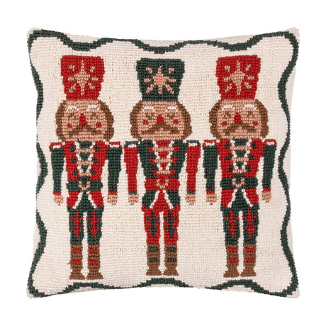 Square tufted cotton cushion featuring three red and green nutcracker soldiers on a cream ground with a scalloped green border, shown against a plain white background.