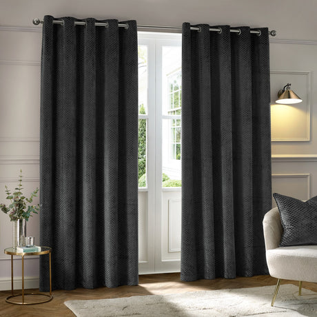 Neptune Velvet Fully Lined Eyelet Curtains in charcoal with raised honeycomb texture, hung as a pair on a metal rod in a living room setting.