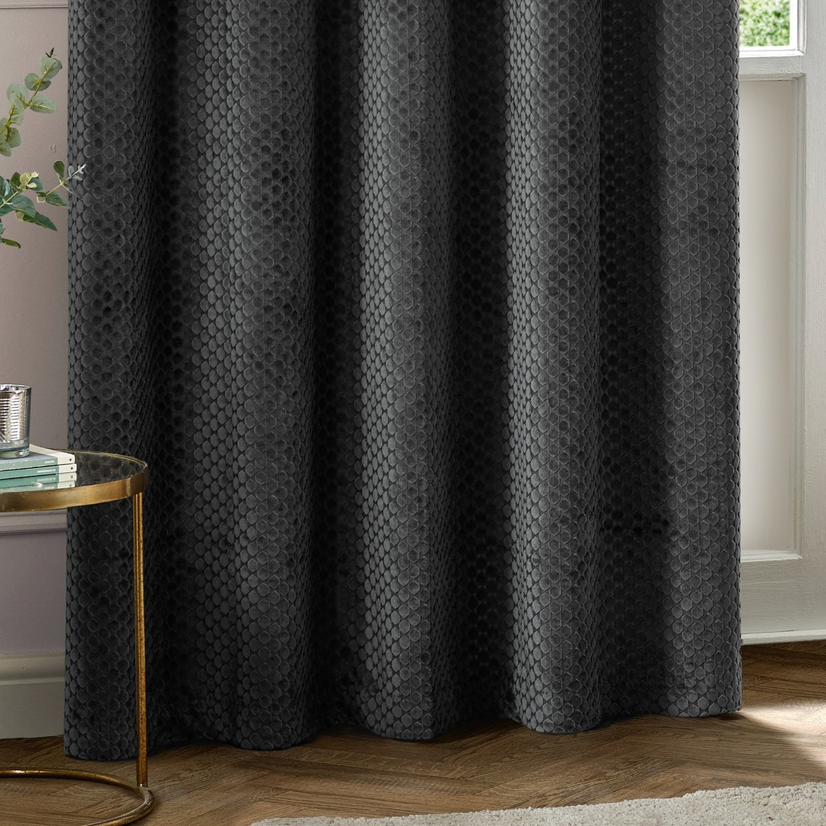 Neptune Velvet Fully Lined Eyelet Curtains in charcoal, showing raised honeycomb-textured fabric with eyelet header, styled in a living room setting.