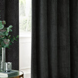 Neptune Velvet Fully Lined Eyelet Curtains in charcoal, showing raised honeycomb-textured fabric hung beside a window in a living room setting.